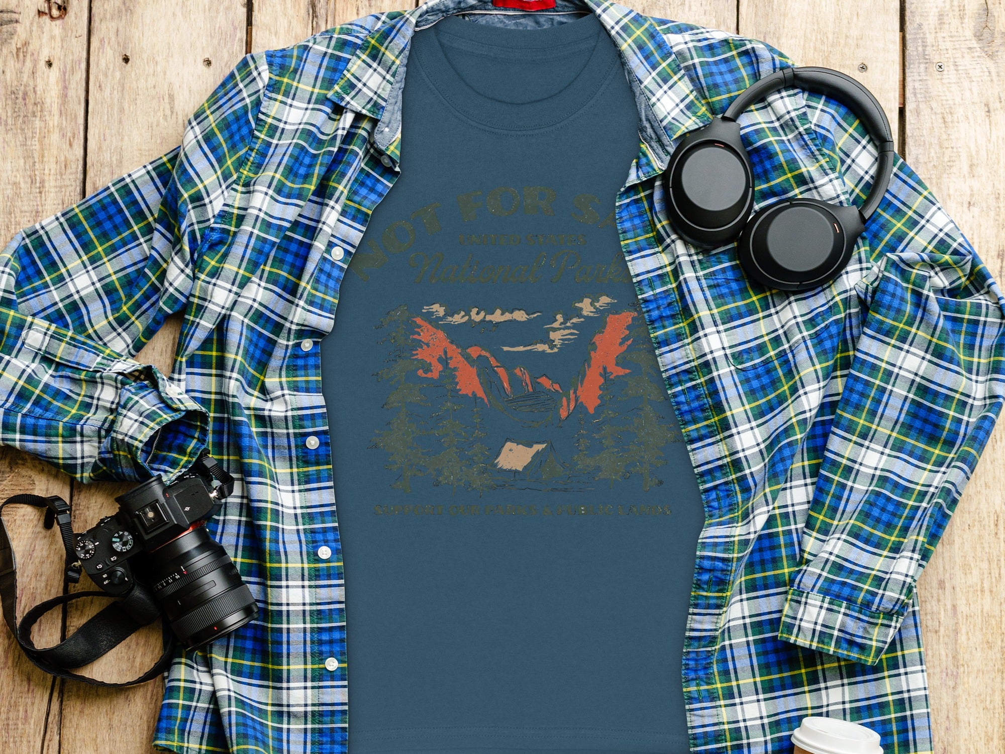 Blue t-shirt with "National Park" graphic and plaid shirt, headphones, and camera.