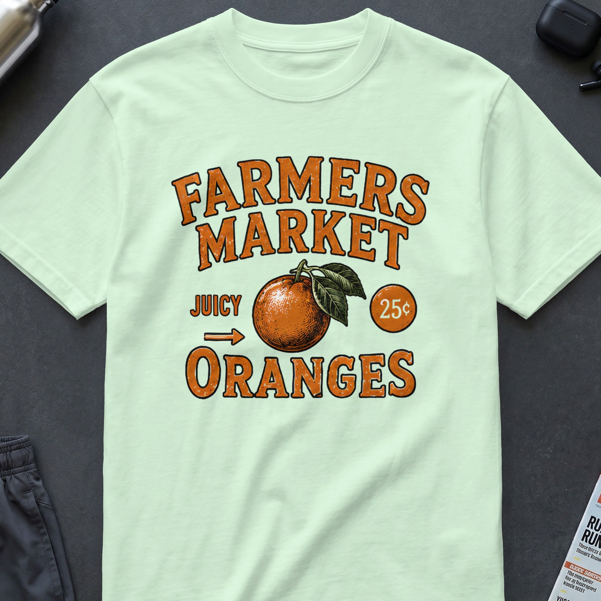 Farmers Market Juicy Oranges graphic on a light green t-shirt.