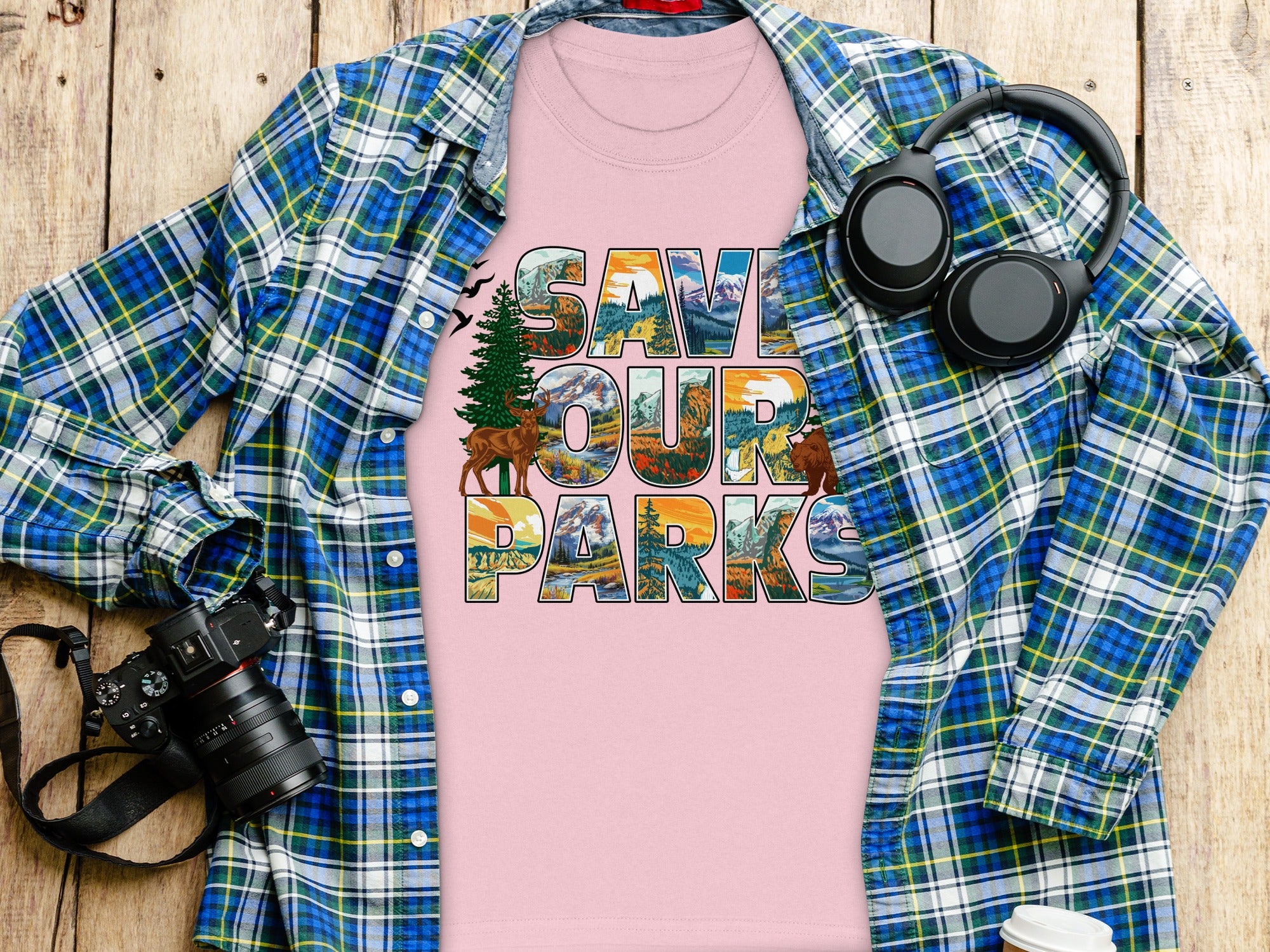 Pink t-shirt with "Save Our Parks" text featuring nature scenes, folded over plaid shirt.