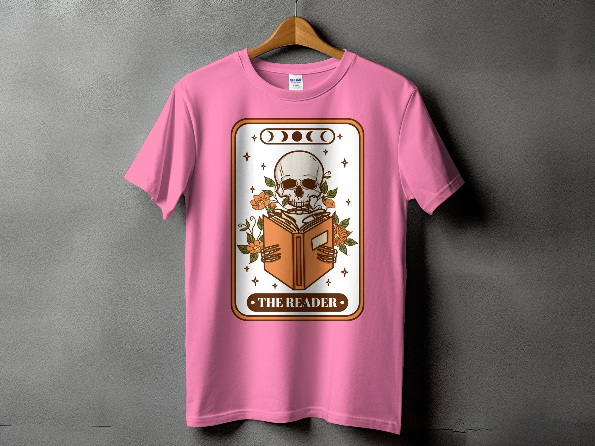 Pink t-shirt with a skeleton reading a book graphic and text "The Reader".