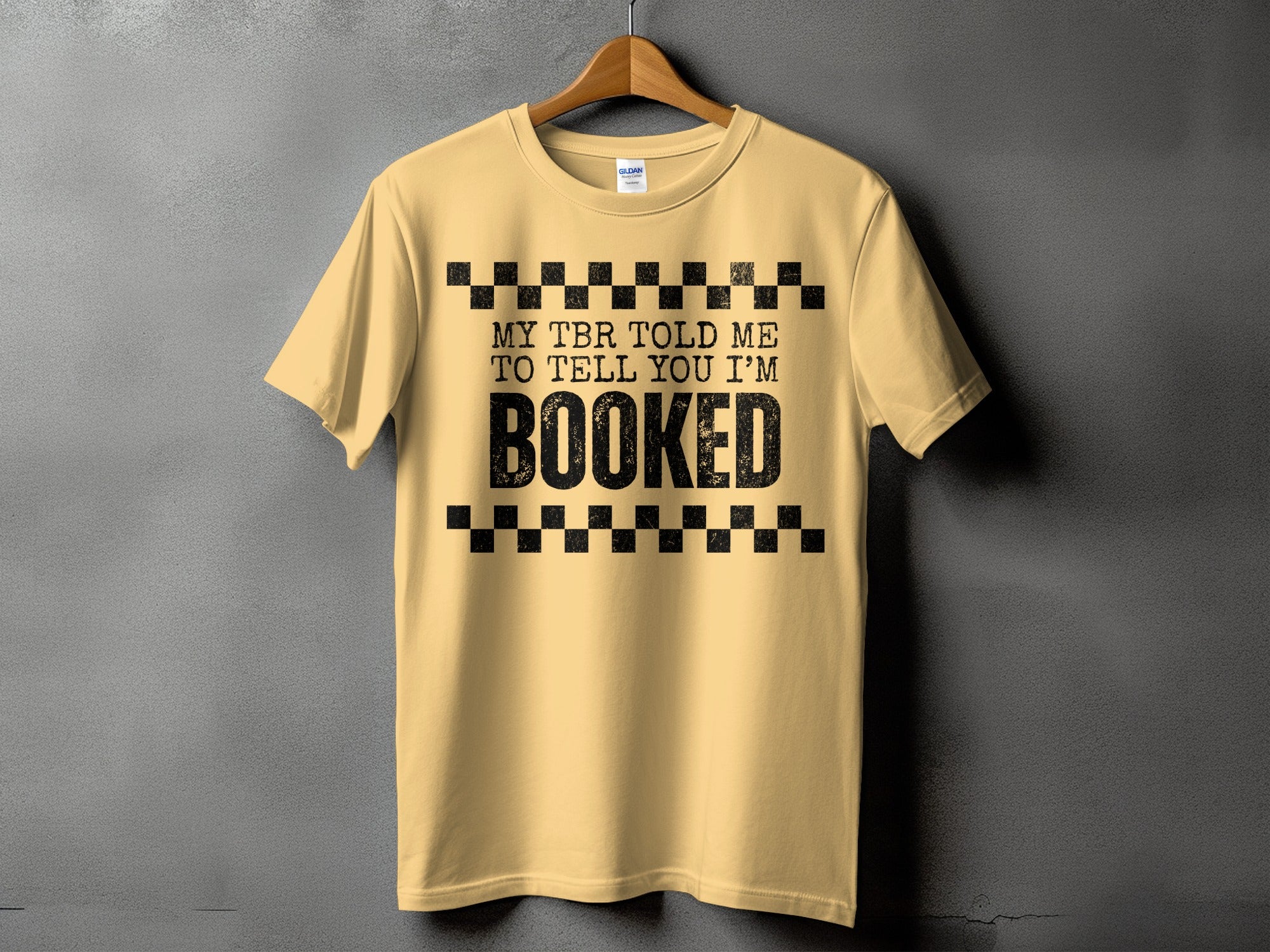 Light yellow t-shirt with black text that reads "MY TBR TOLD ME TO TELL YOU I'M BOOKED".