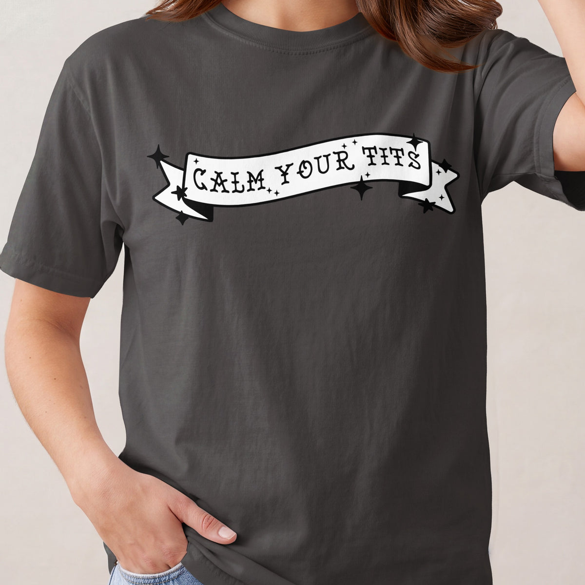 Dark gray t-shirt with white banner graphic reading "CALM YOUR TITS".
