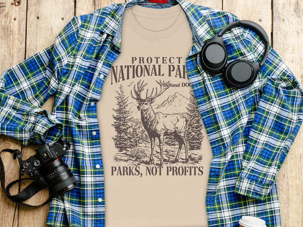 Beige t-shirt with deer and mountains graphic, "Protect National Parks, Not Profits".