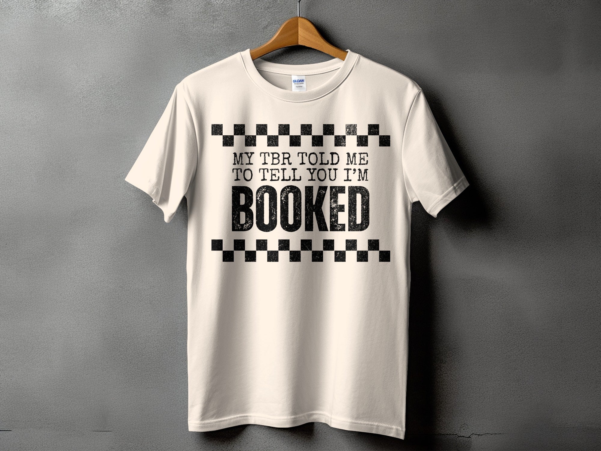 Light cream t-shirt with black text that reads "MY TBR TOLD ME TO TELL YOU I'M BOOKED".