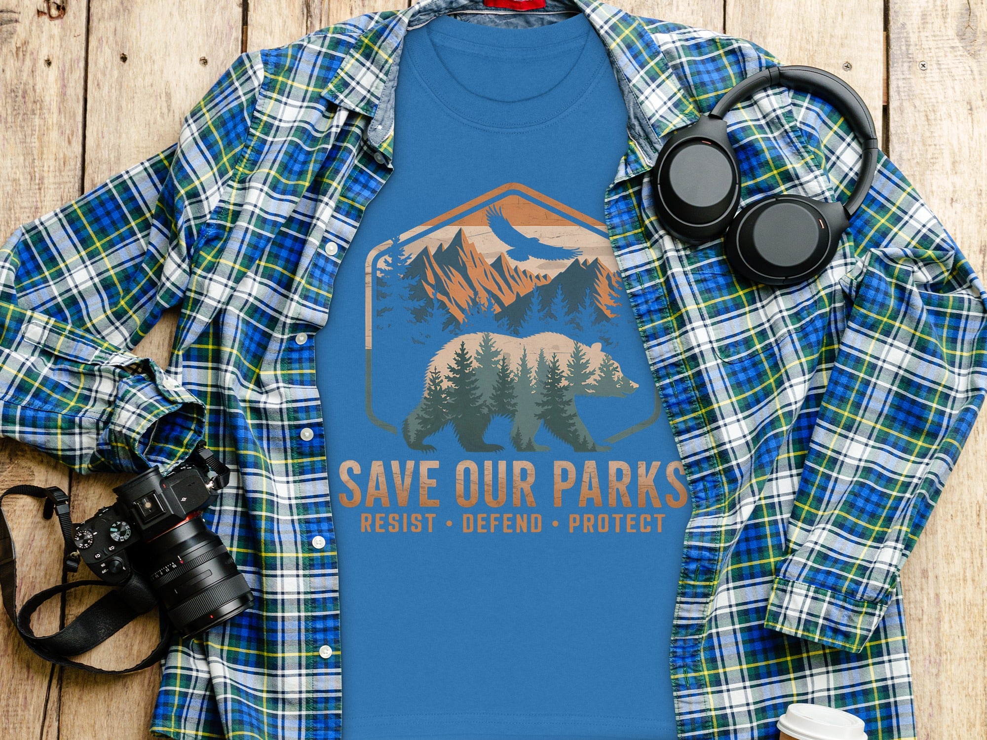 Blue t-shirt with bear graphic and "Save Our Parks" text, laid on a wooden surface.
