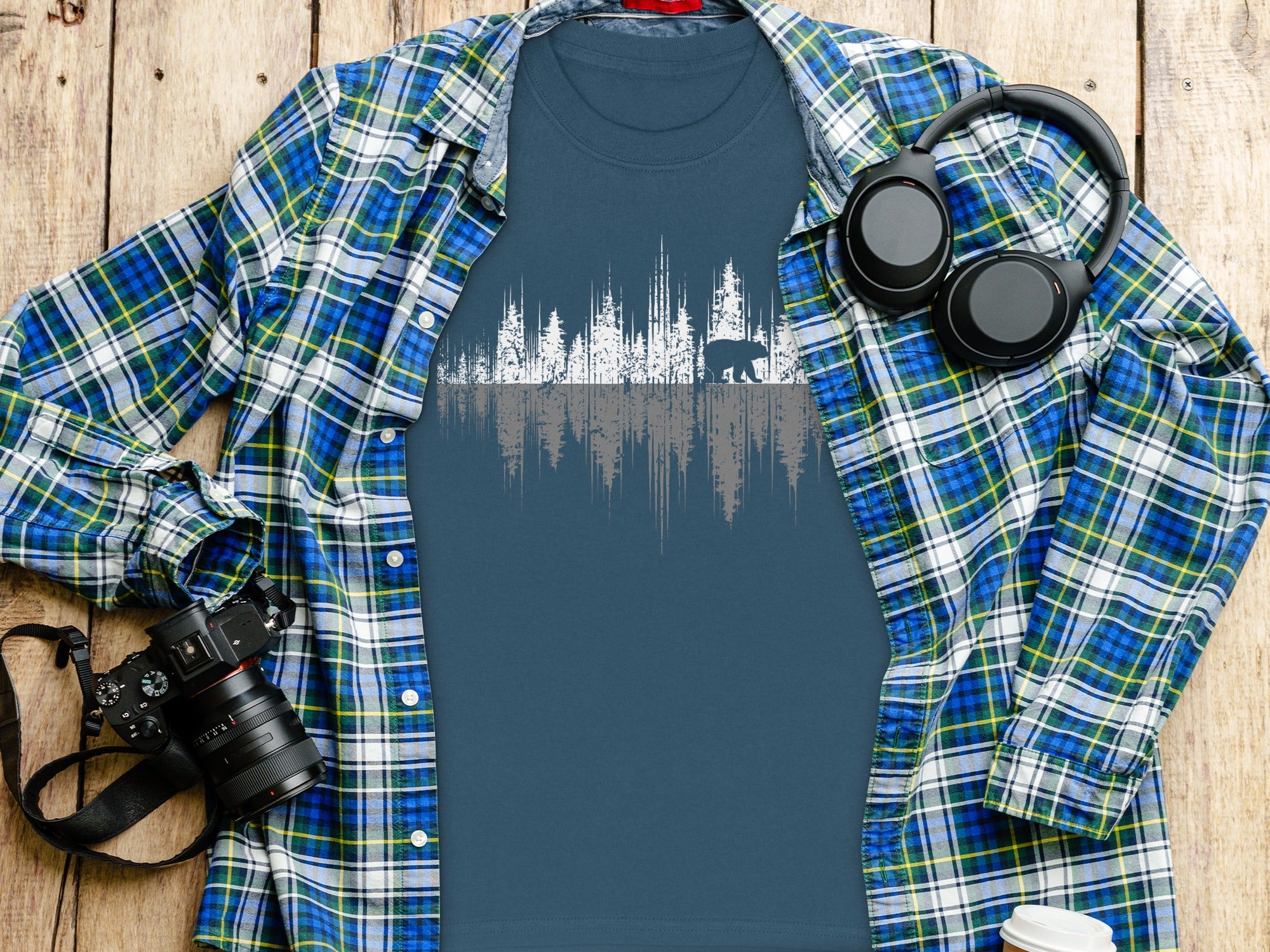 Blue t-shirt with white and gray forest and bear graphic, worn under plaid shirt.