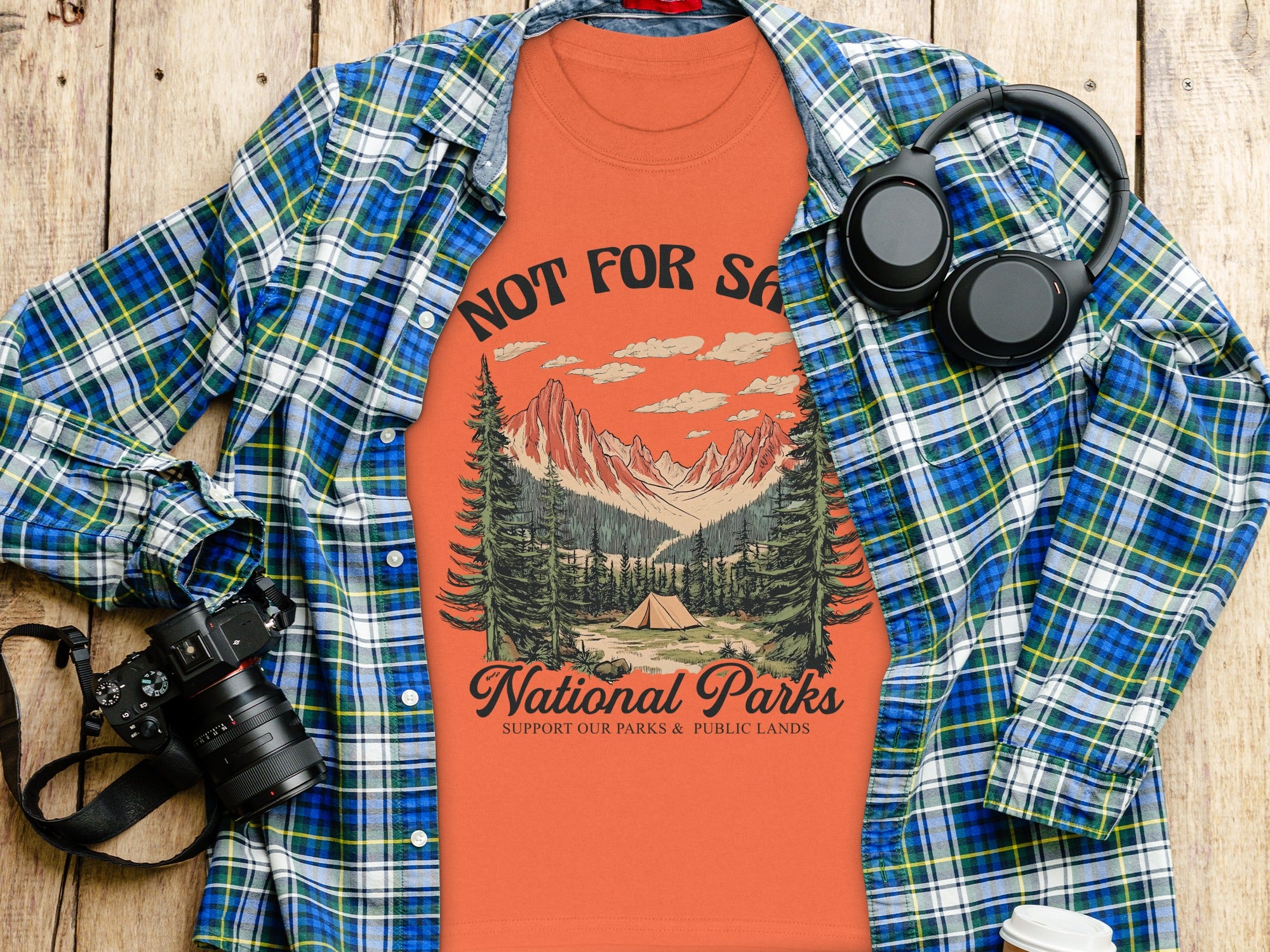 Orange t-shirt with "National Parks" design, plaid shirt, headphones, and camera.