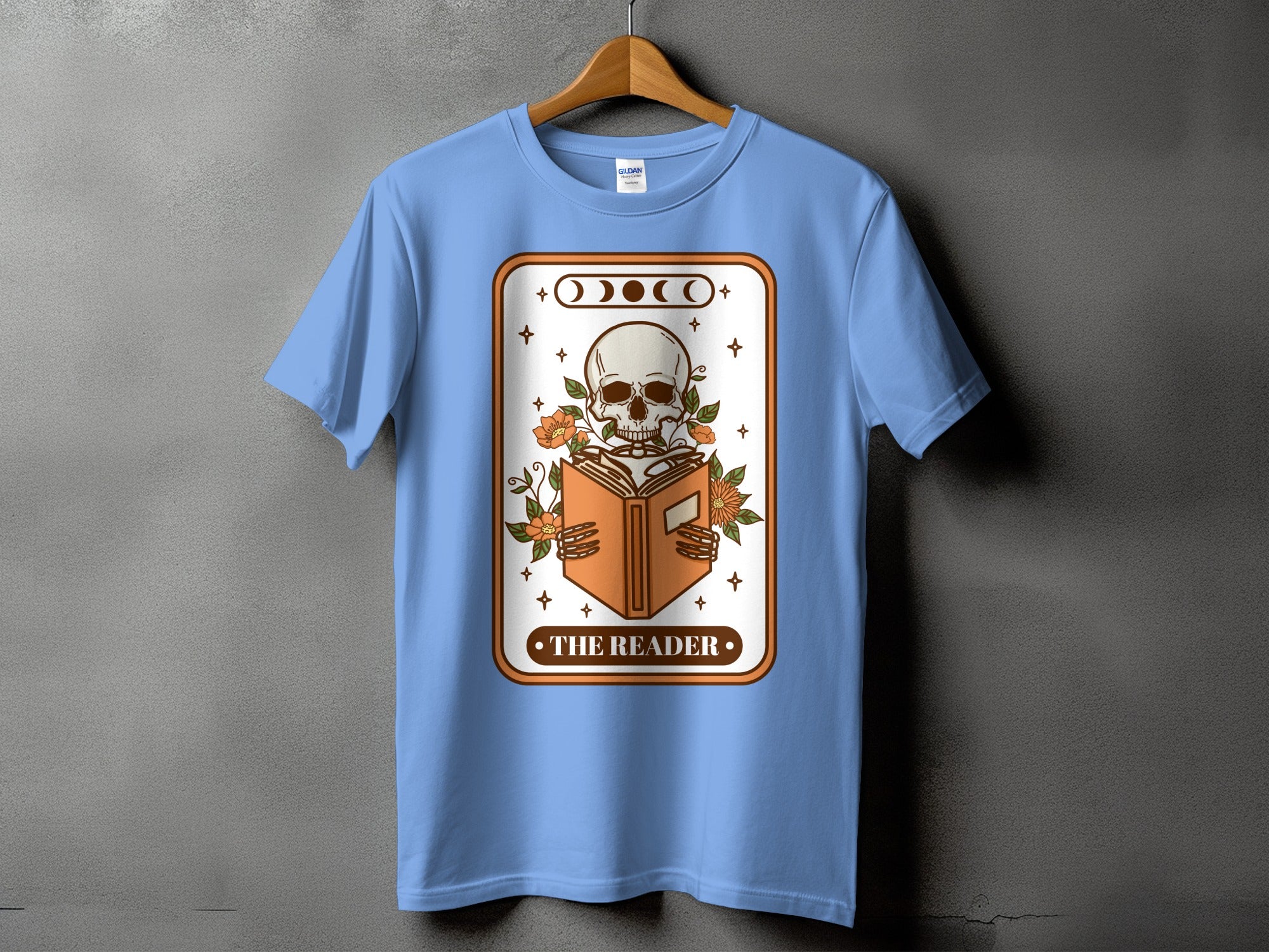Light blue t-shirt with a skeleton reading a book graphic and text "The Reader".