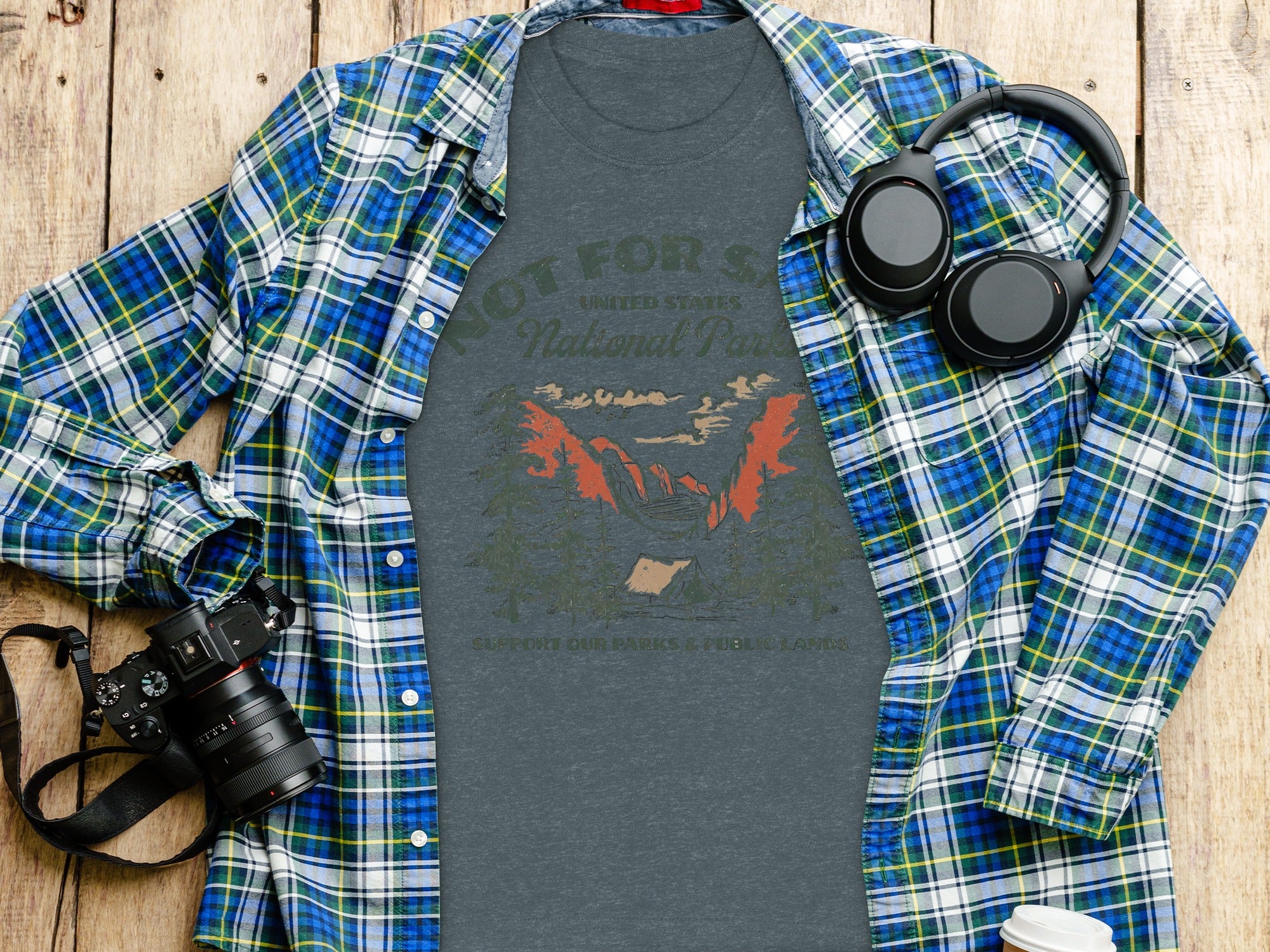 Charcoal t-shirt with National Parks graphic, layered with plaid shirt, camera, headphones, and coffee cup.