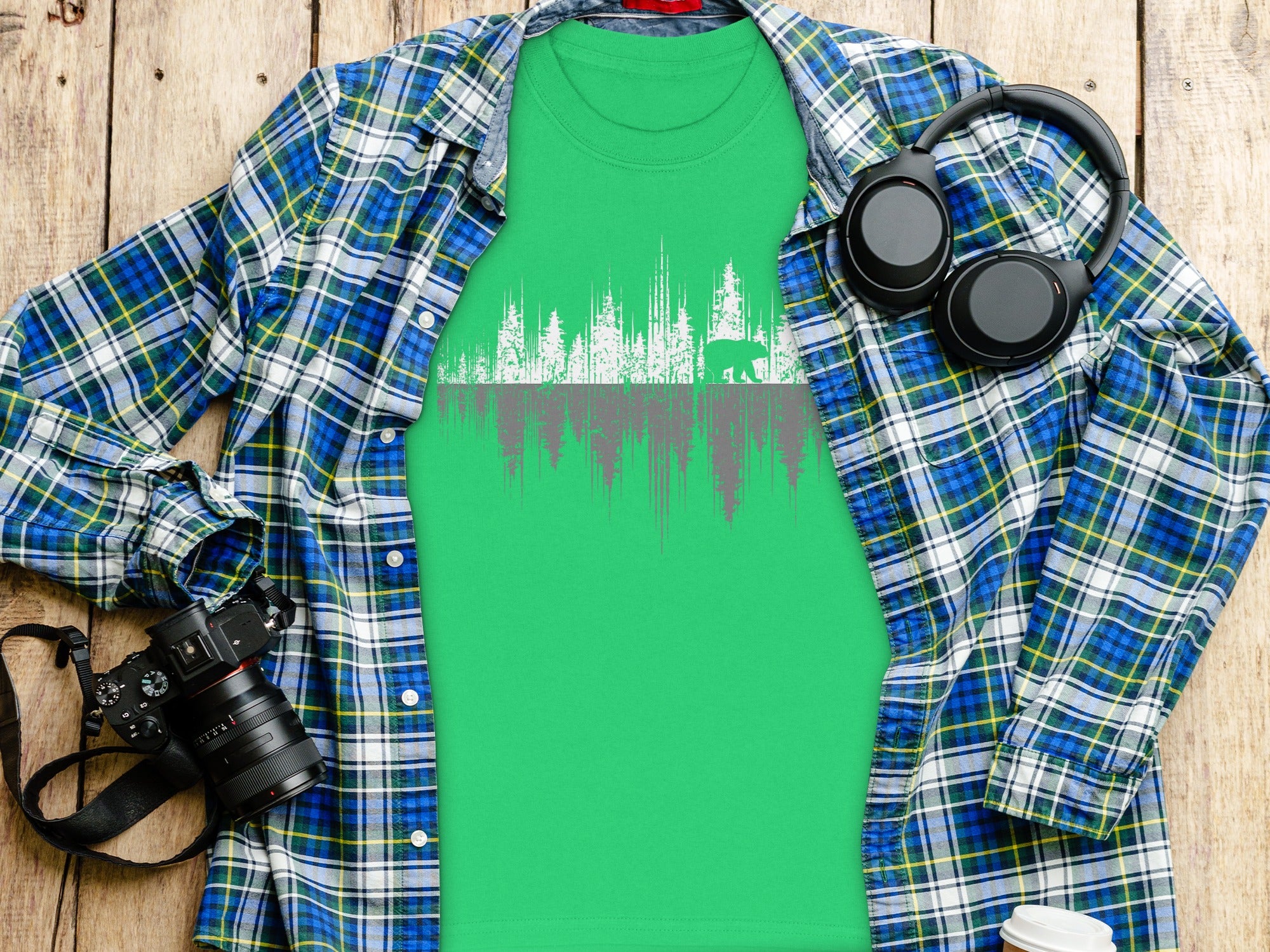 Green t-shirt with white and gray forest and bear graphic, laid flat with flannel shirt.