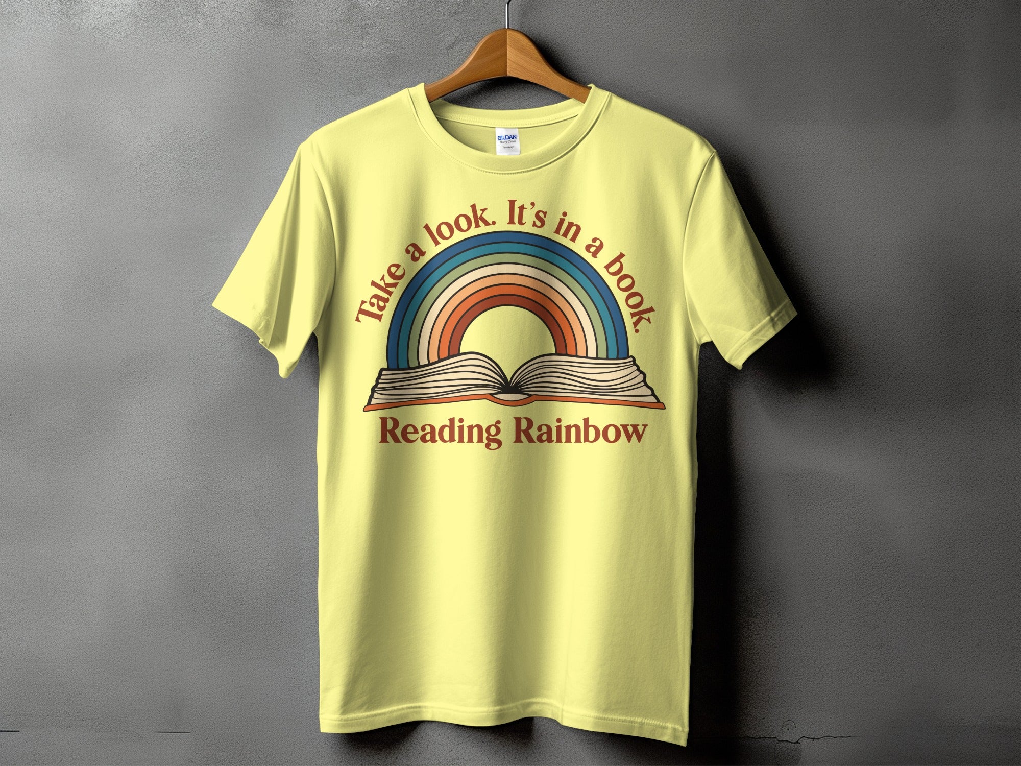 Yellow t-shirt with "Take a look. It's in a book" and a rainbow over an open book.