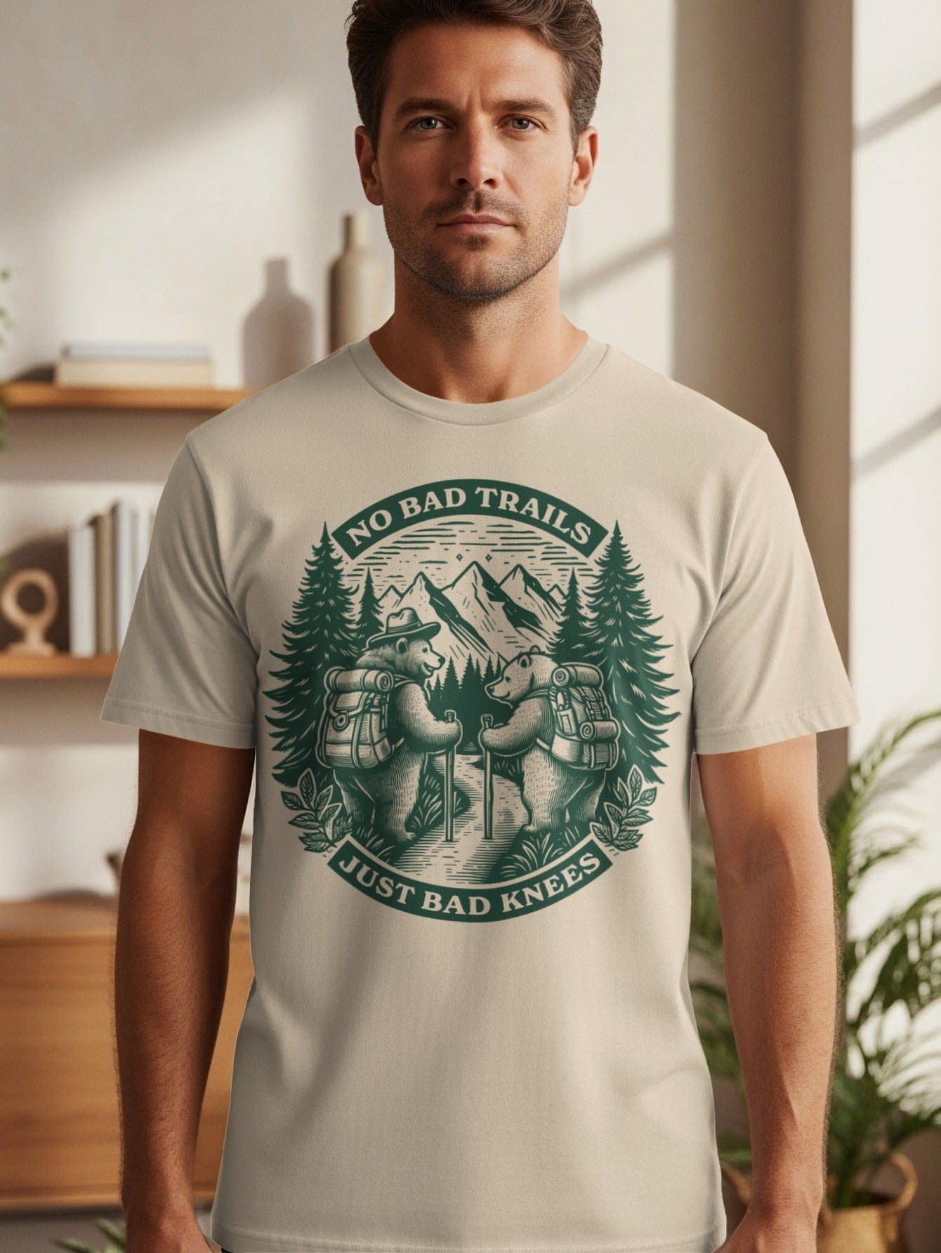 Light t-shirt with green graphic of two bears hiking, mountains, and text "NO BAD TRAILS JUST BAD KNEES".