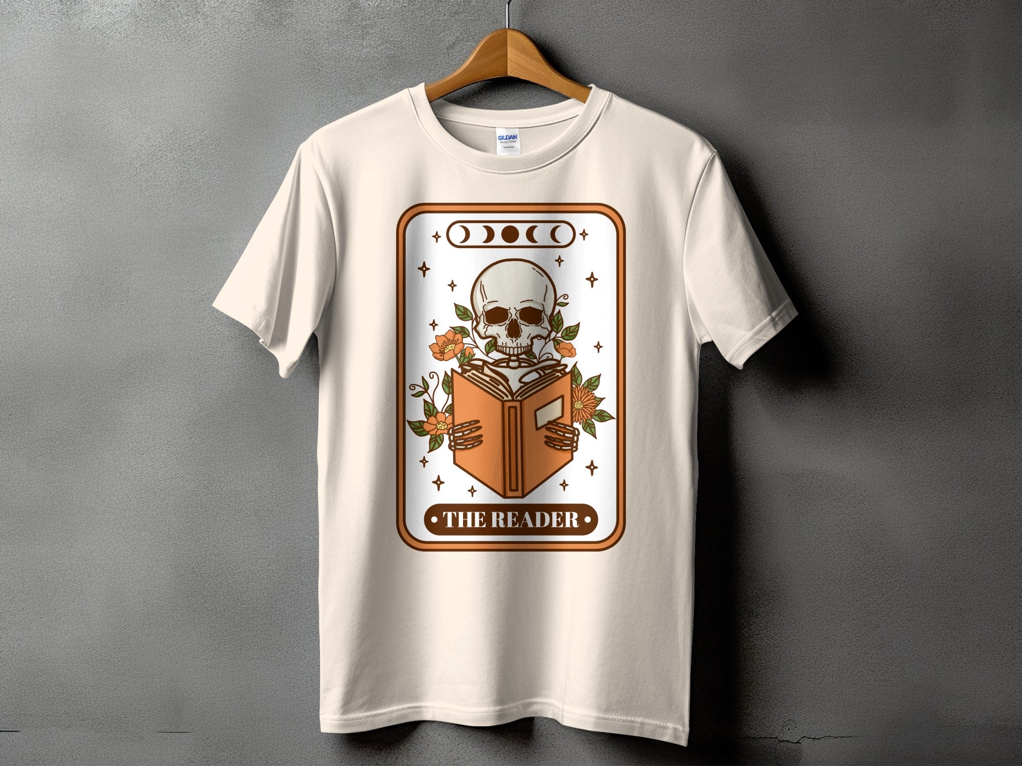 Cream t-shirt with skeleton reading a book, moon phases, and "The Reader" text.