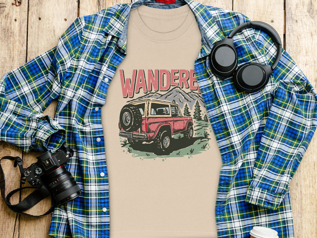 T-shirt with "WANDERE" text and vintage SUV graphic, layed flat with flannel shirt.