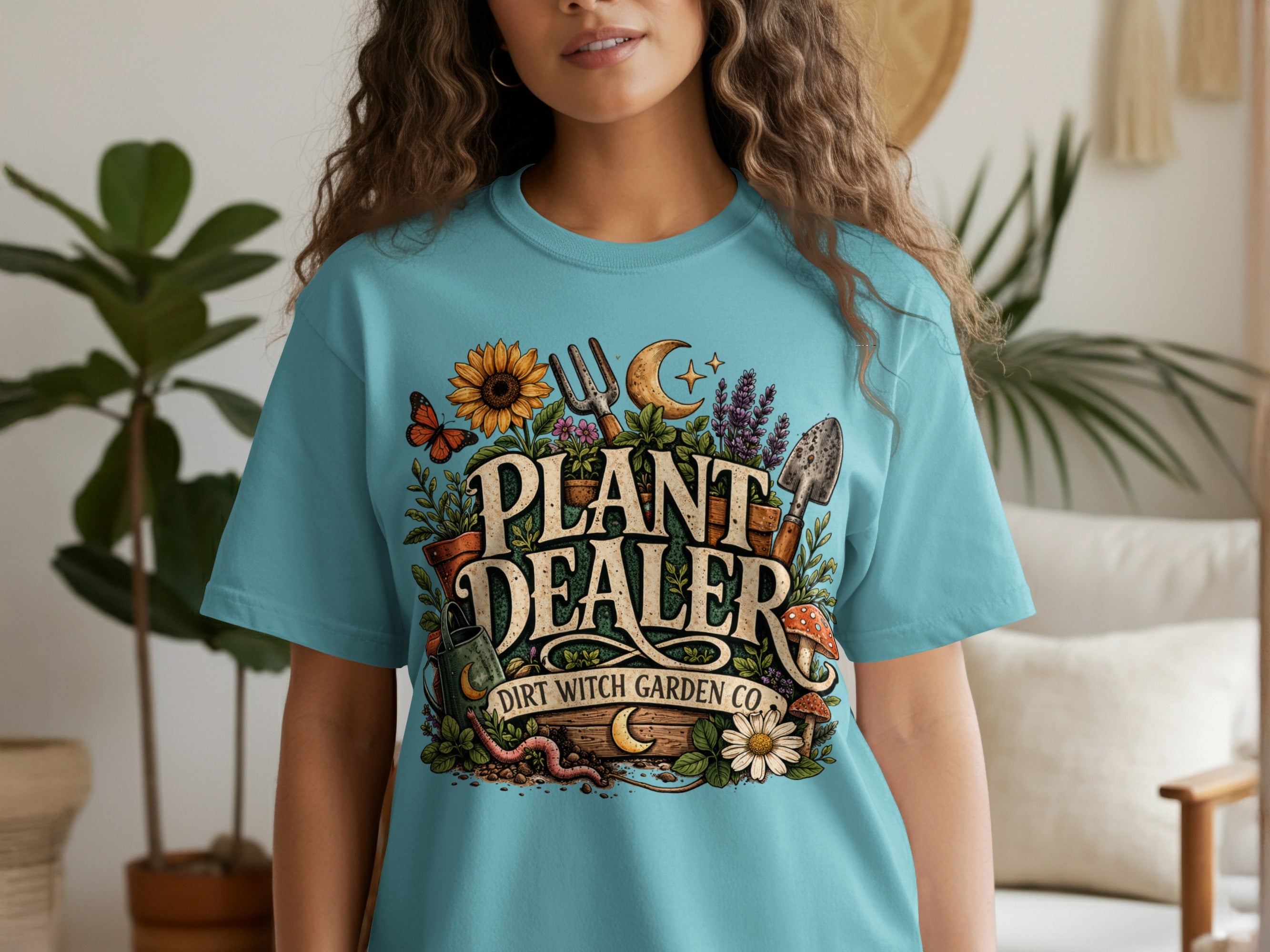 Cyan t-shirt featuring "PLANT DEALER DIRT WITCH GARDEN CO." text with gardening and nature graphics.