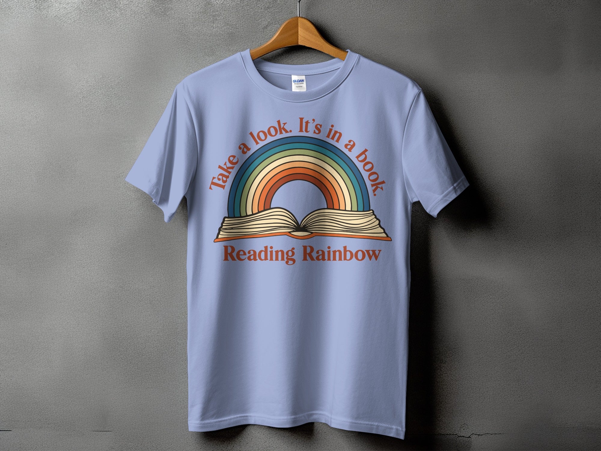 Light blue t-shirt with a rainbow arching over an open book, text reads "Take a look. It's in a book Reading Rainbow".