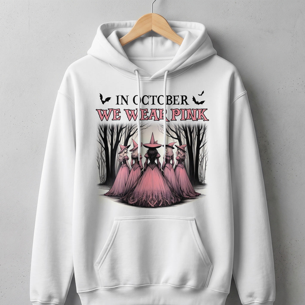 White hoodie with "In October We Wear Pink" text and witches in a forest.