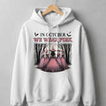 White hoodie with "In October We Wear Pink" text and witches in a forest.