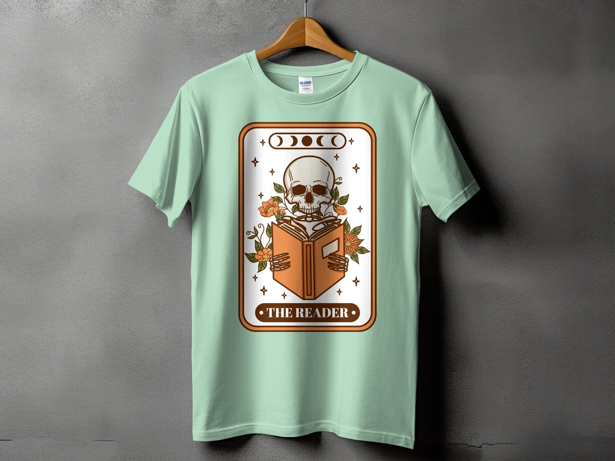 Light green t-shirt with graphic of skeleton reading a book and text "THE READER".