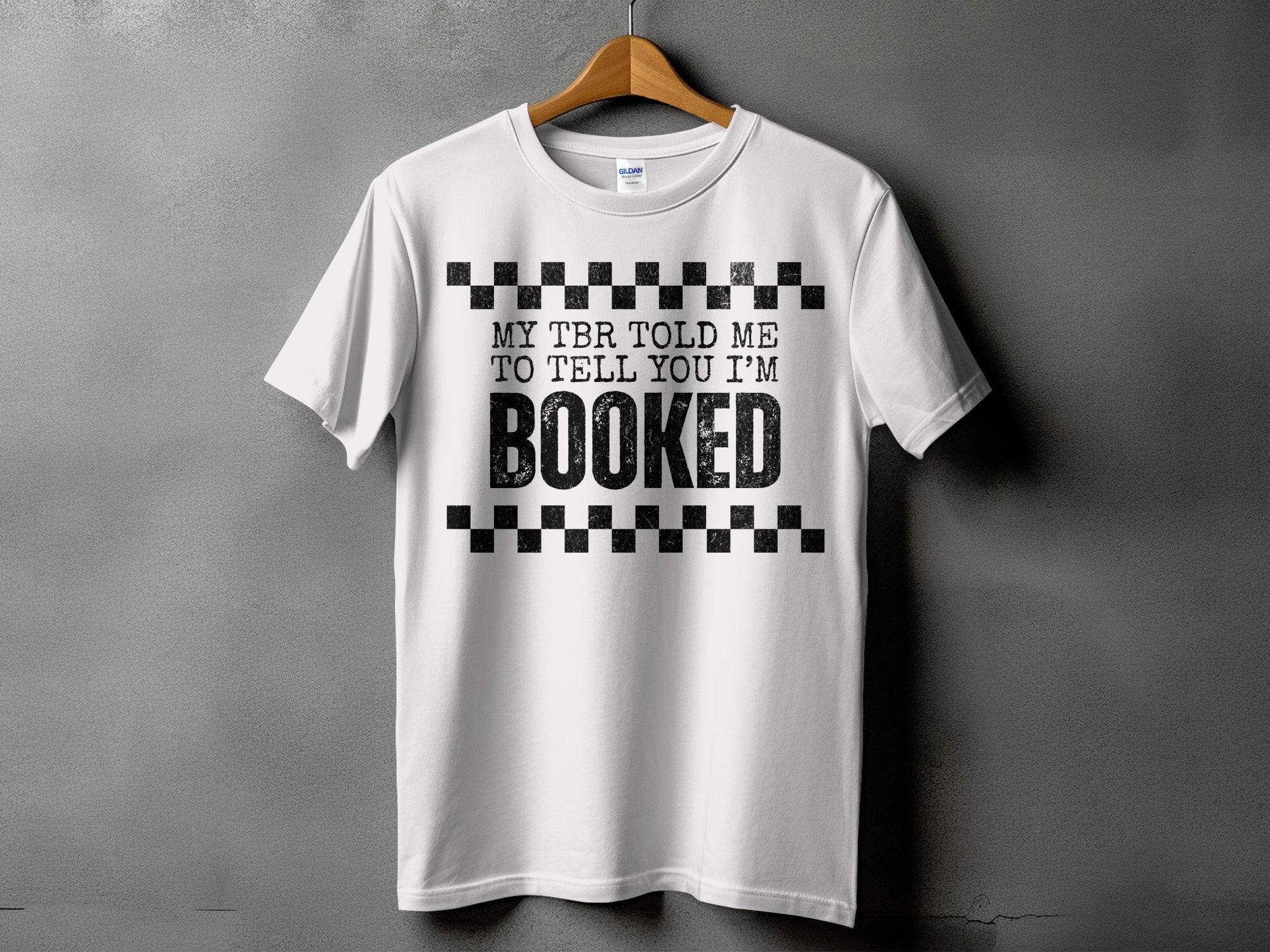 White t-shirt with black checkerboard pattern and text "MY TBR TOLD ME TO TELL YOU I'M BOOKED".
