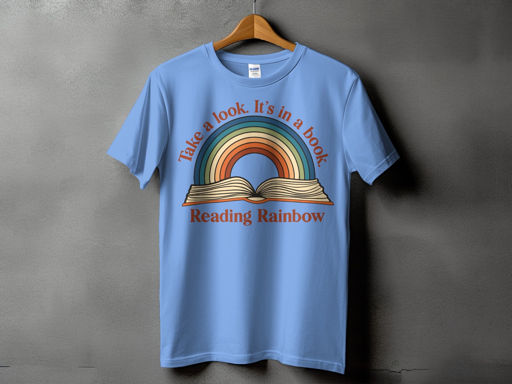 Light blue t-shirt with a rainbow and open book graphic reading "Take a look. It's in a book."