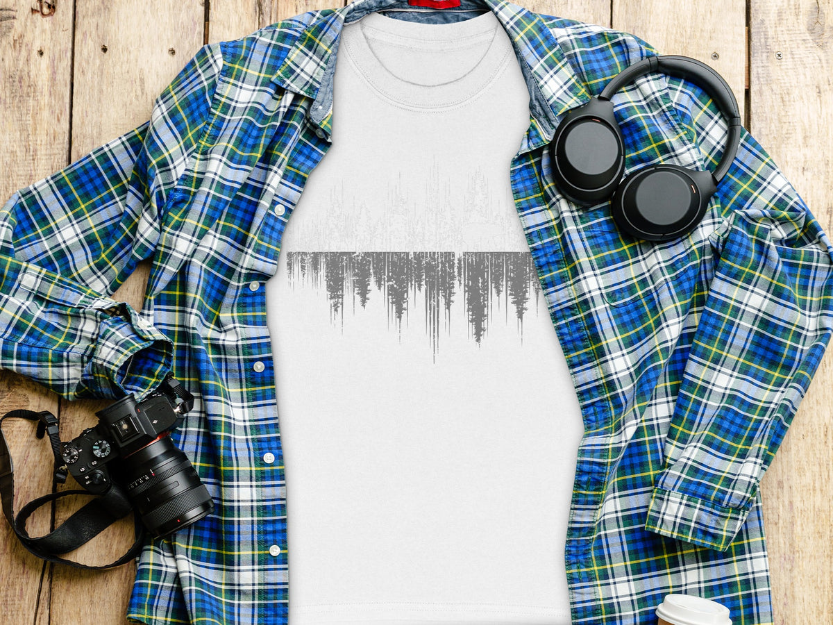 White t-shirt with grey abstract forest graphic, blue plaid shirt, headphones, camera.