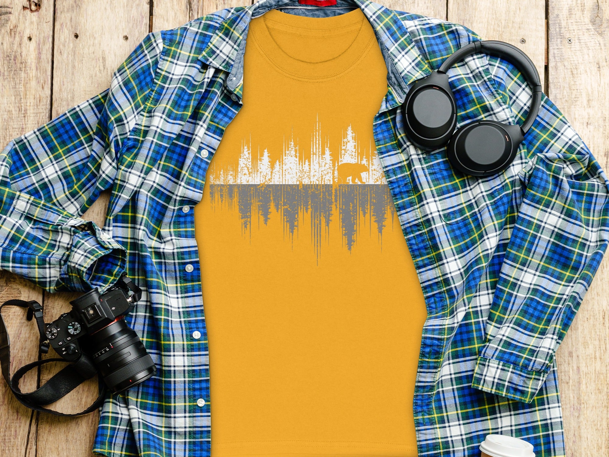 Orange t-shirt with forest and bear graphic, plaid shirt, camera, and headphones.