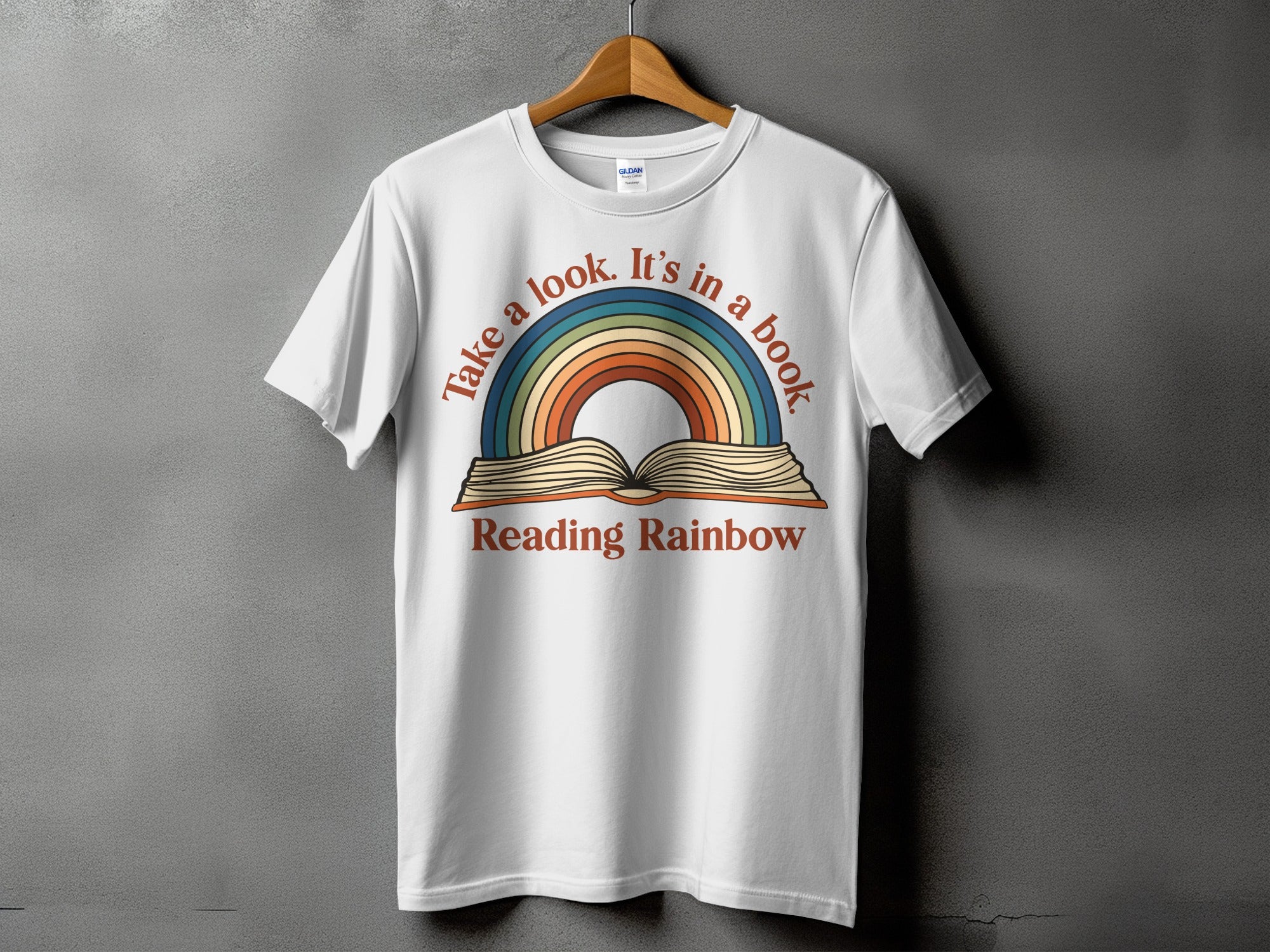 White t-shirt with "Take a look. It's in a book Reading Rainbow" text and rainbow graphic.