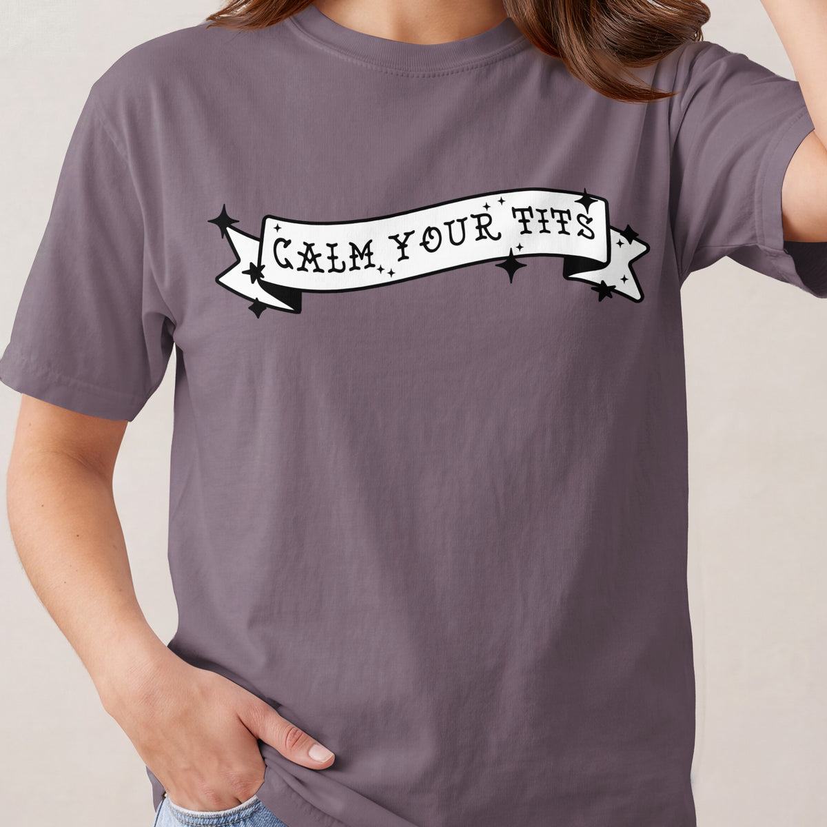 Purple t-shirt with white banner graphic reading "CALM YOUR TITS".