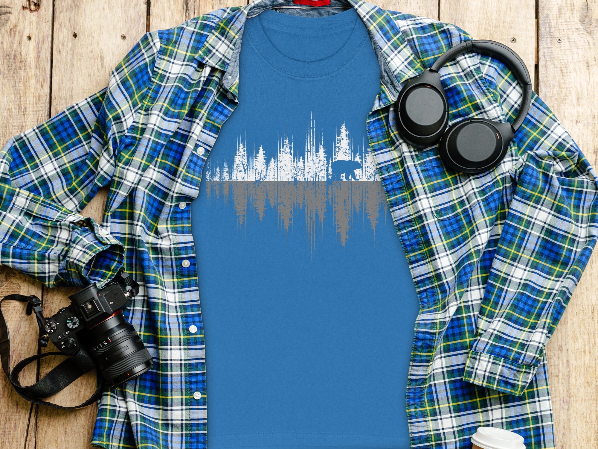 Blue t-shirt with white and grey forest and bear graphic, layered under plaid shirt.