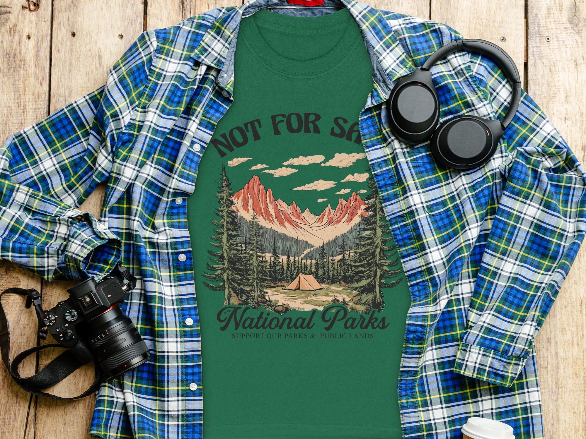 Green t-shirt with landscape graphic and text National Parks, placed on wooden surface.