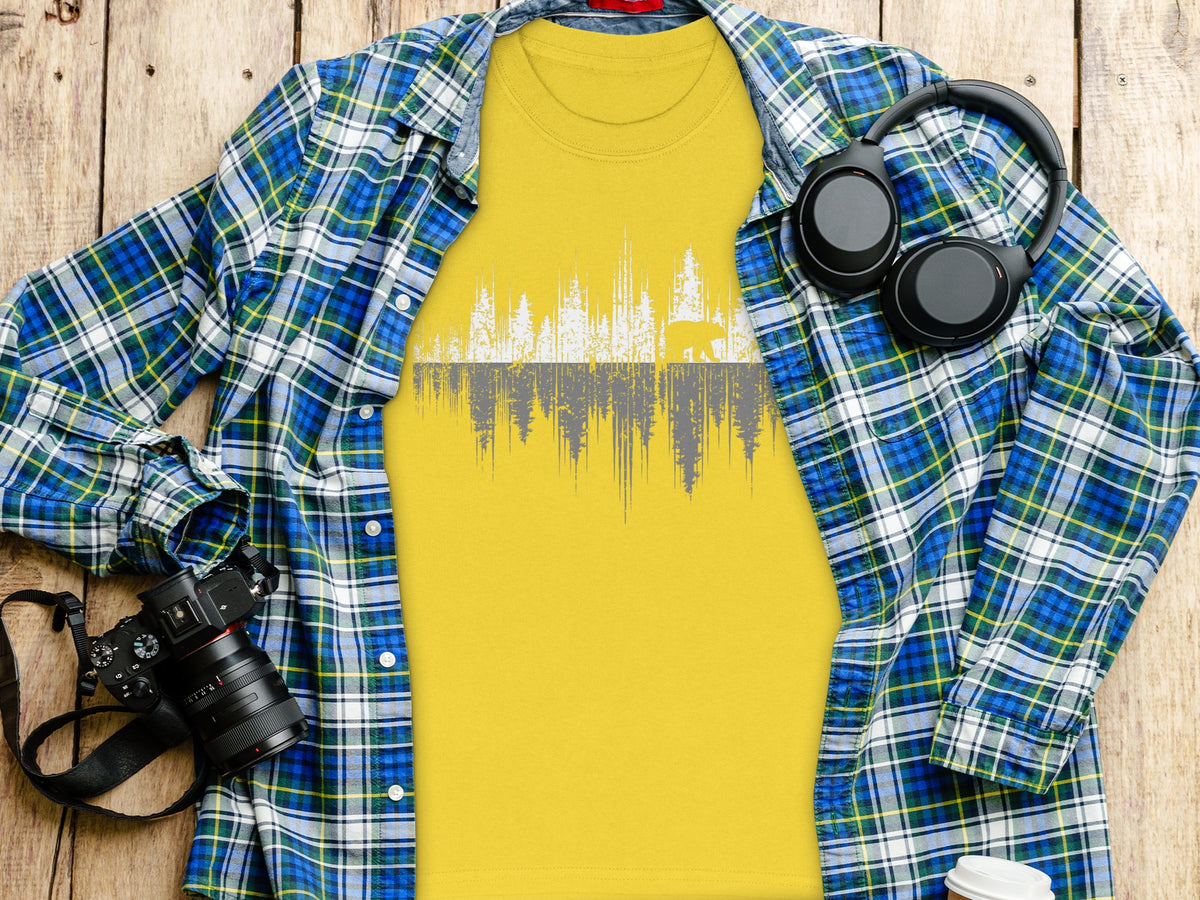 Yellow t-shirt with white and gray forest and bear graphic, spread open over wooden planks.