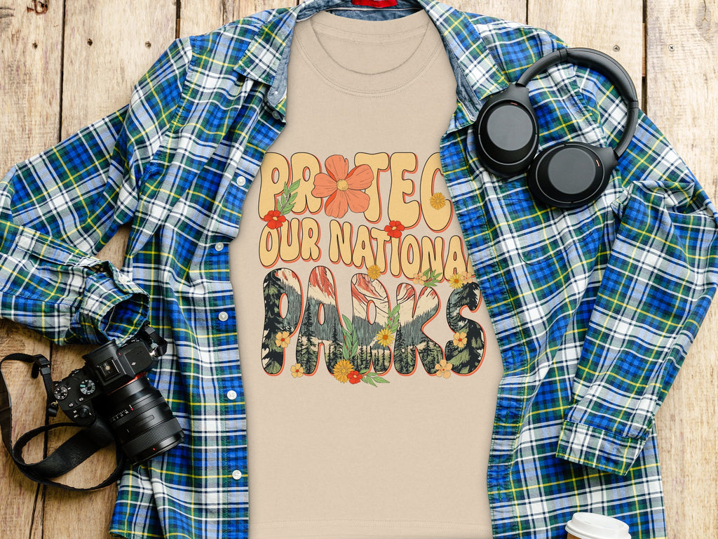 "Protect Our National Parks" text on light beige t-shirt, with flannel shirt, headphones, and camera.