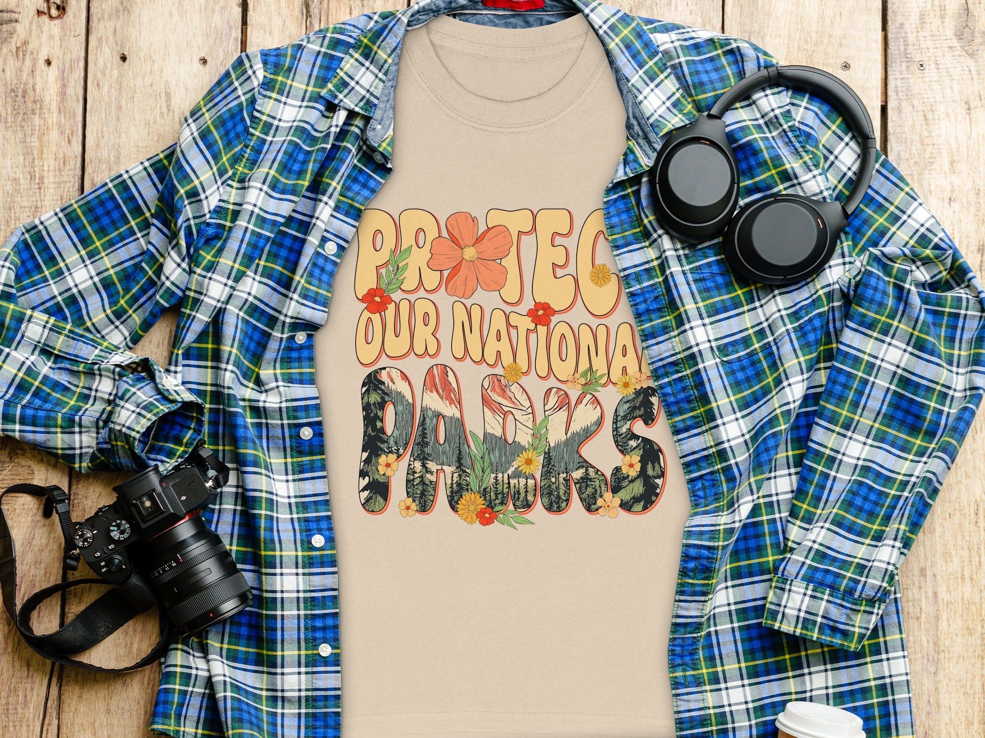 "Protect Our National Parks" text on light beige t-shirt, with flannel shirt, headphones, and camera.
