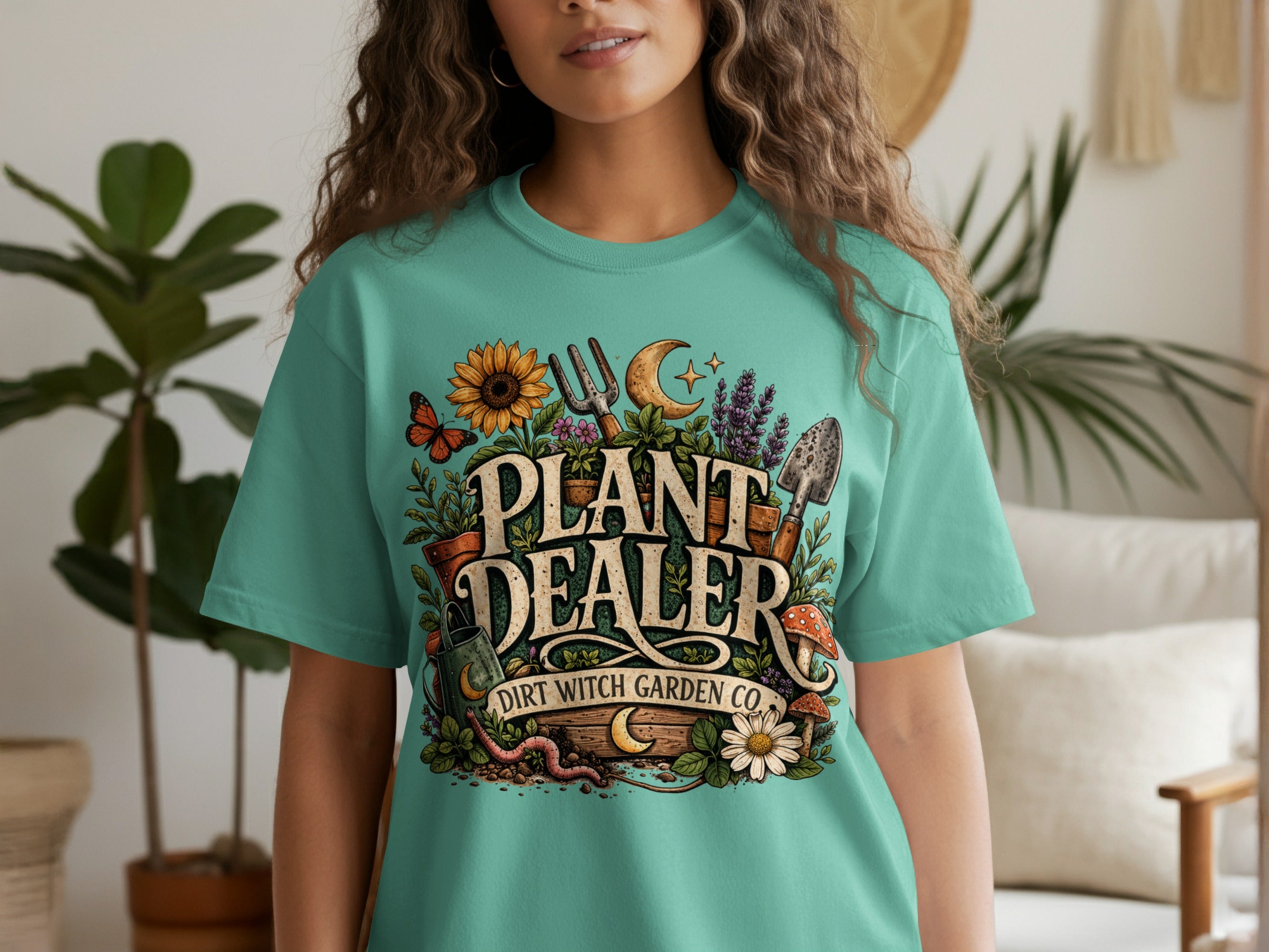 Teal t-shirt with "Plant Dealer Dirt Witch Garden Co." graphic featuring gardening tools and plants.