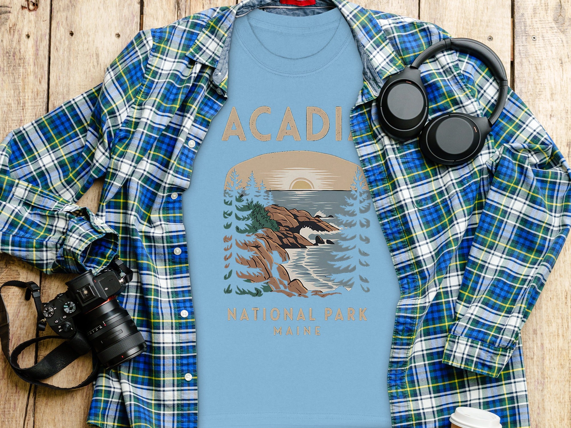Light blue t-shirt with Acadia National Park Maine graphic, plaid shirt, headphones, and camera.