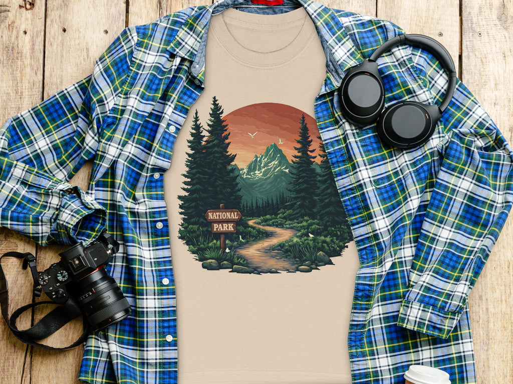 T-shirt with national park graphic, camera, headphones, and coffee cup on wooden surface.