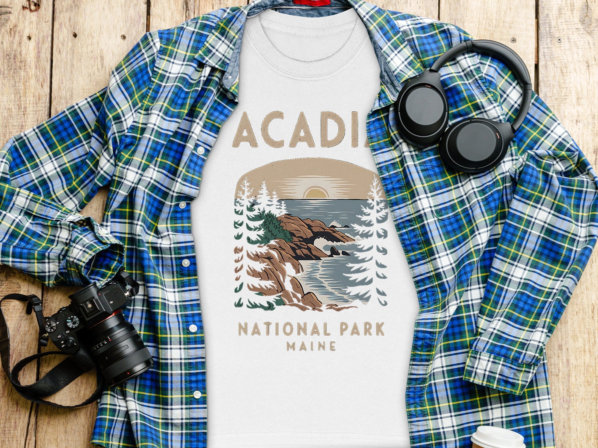 Acadia National Park Maine graphic t-shirt with plaid shirt, camera, and headphones.
