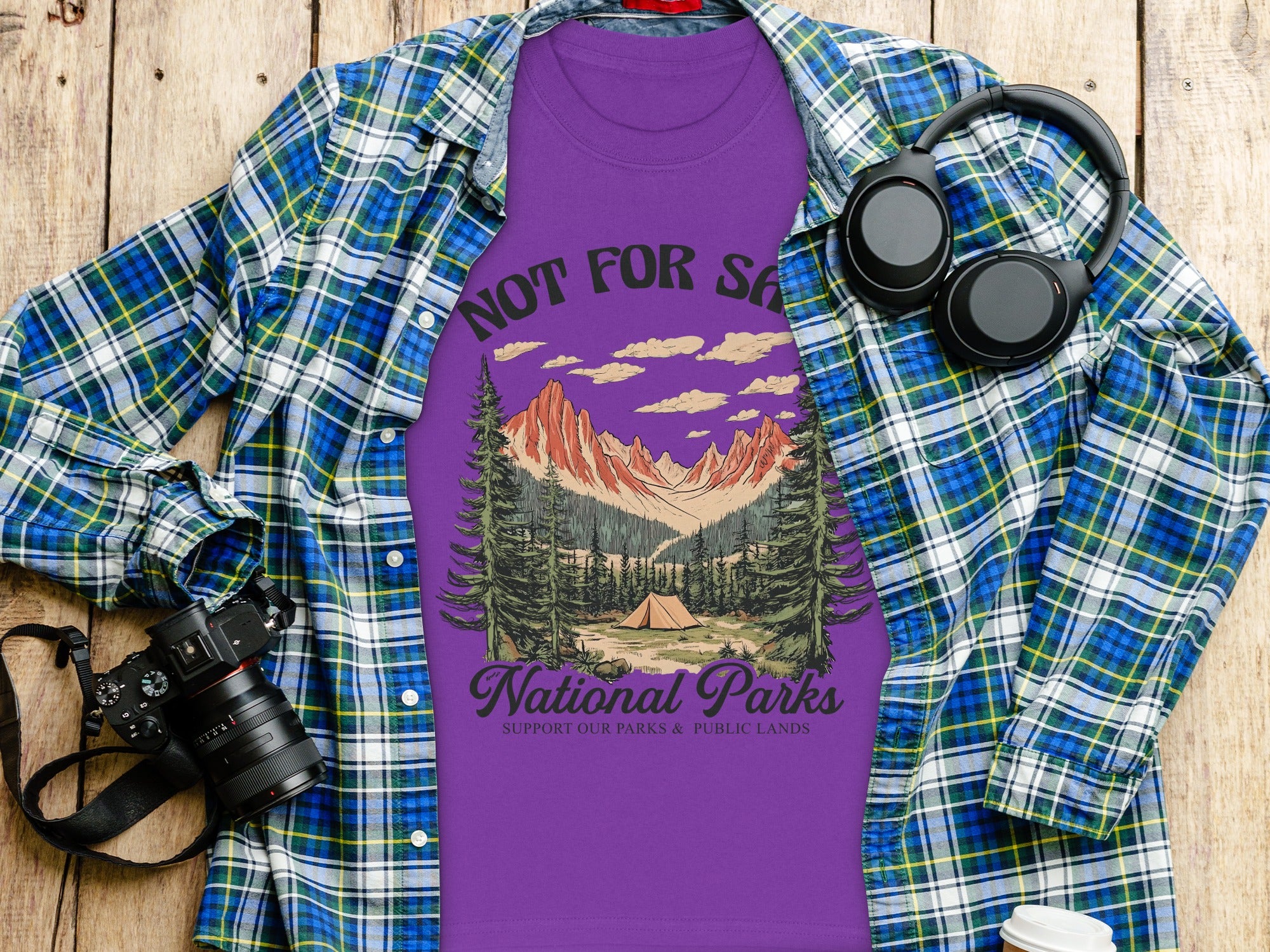 Purple t-shirt with "Not For Sasha" and a mountain landscape, over a plaid shirt.