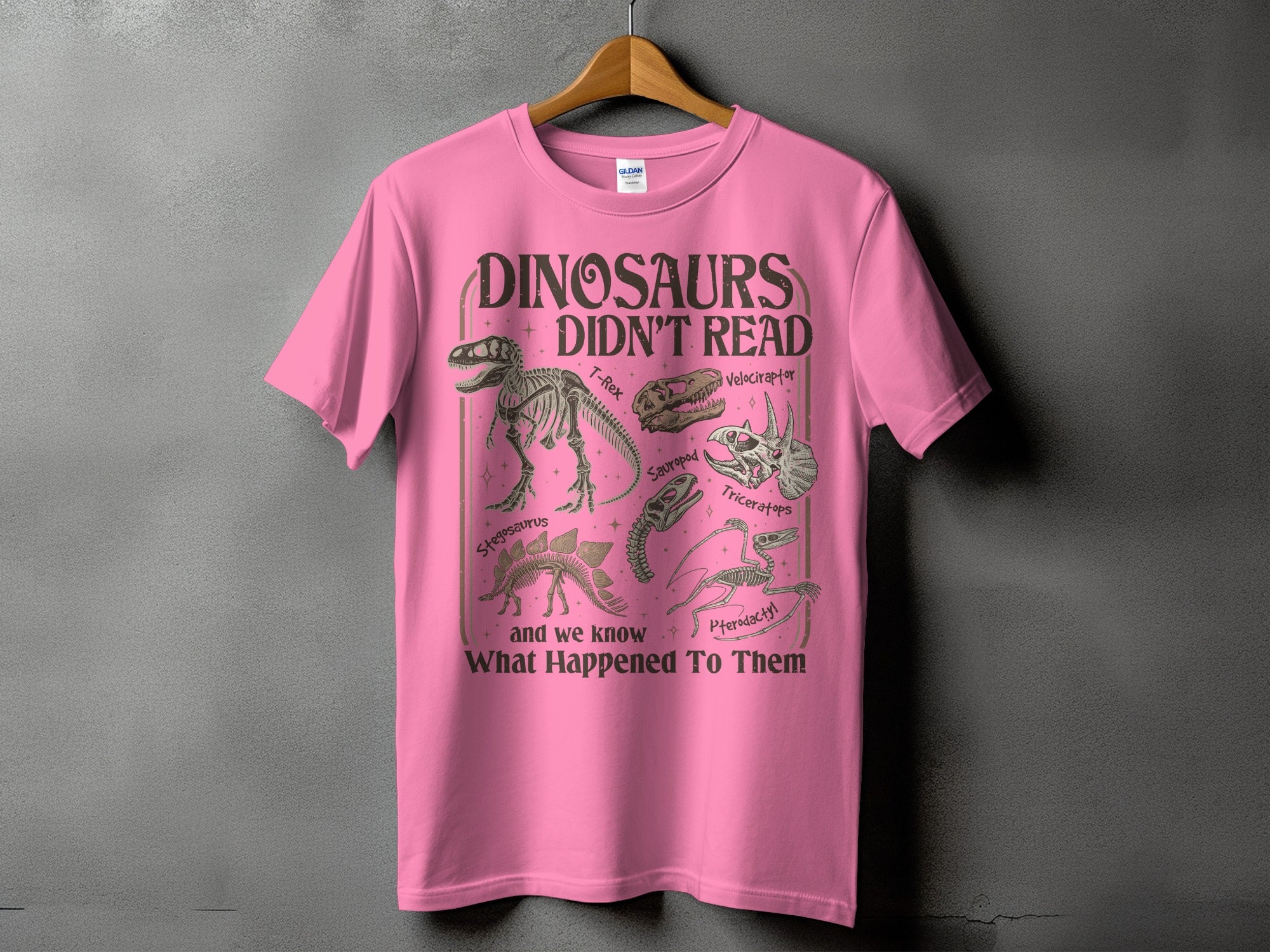 Pink t-shirt with "Dinosaurs Didn't Read" and dinosaur skeletons print.