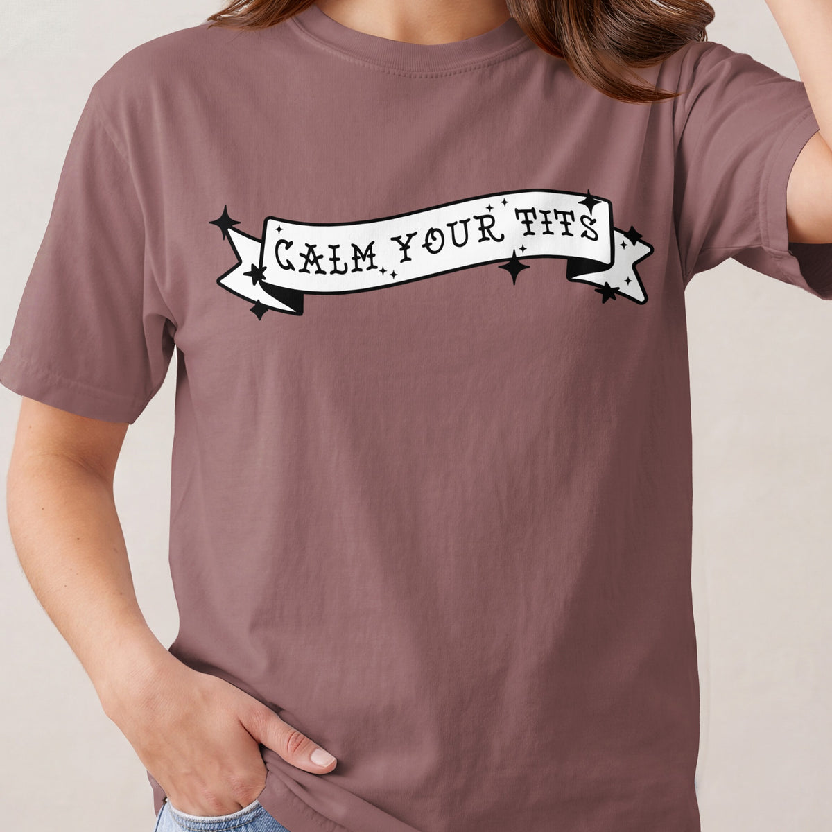 Brown t-shirt with a banner graphic that says "CALM YOUR TITS".