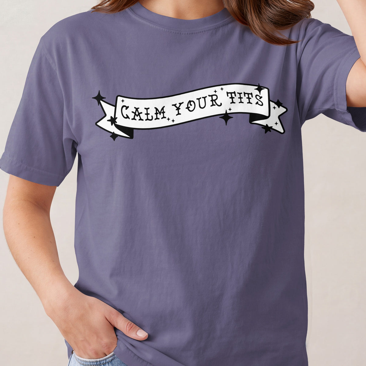 Purple t-shirt with a white banner graphic that says "CALM YOUR TITS"