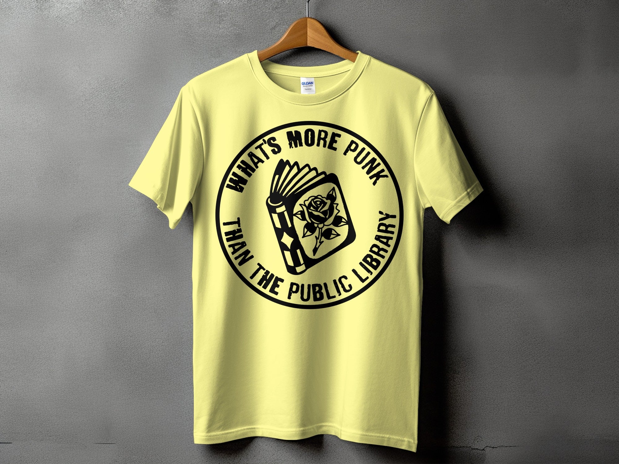 Yellow t-shirt with black circular graphic featuring an open book and rose, text reads "What's More Punk Than The Public Library".
