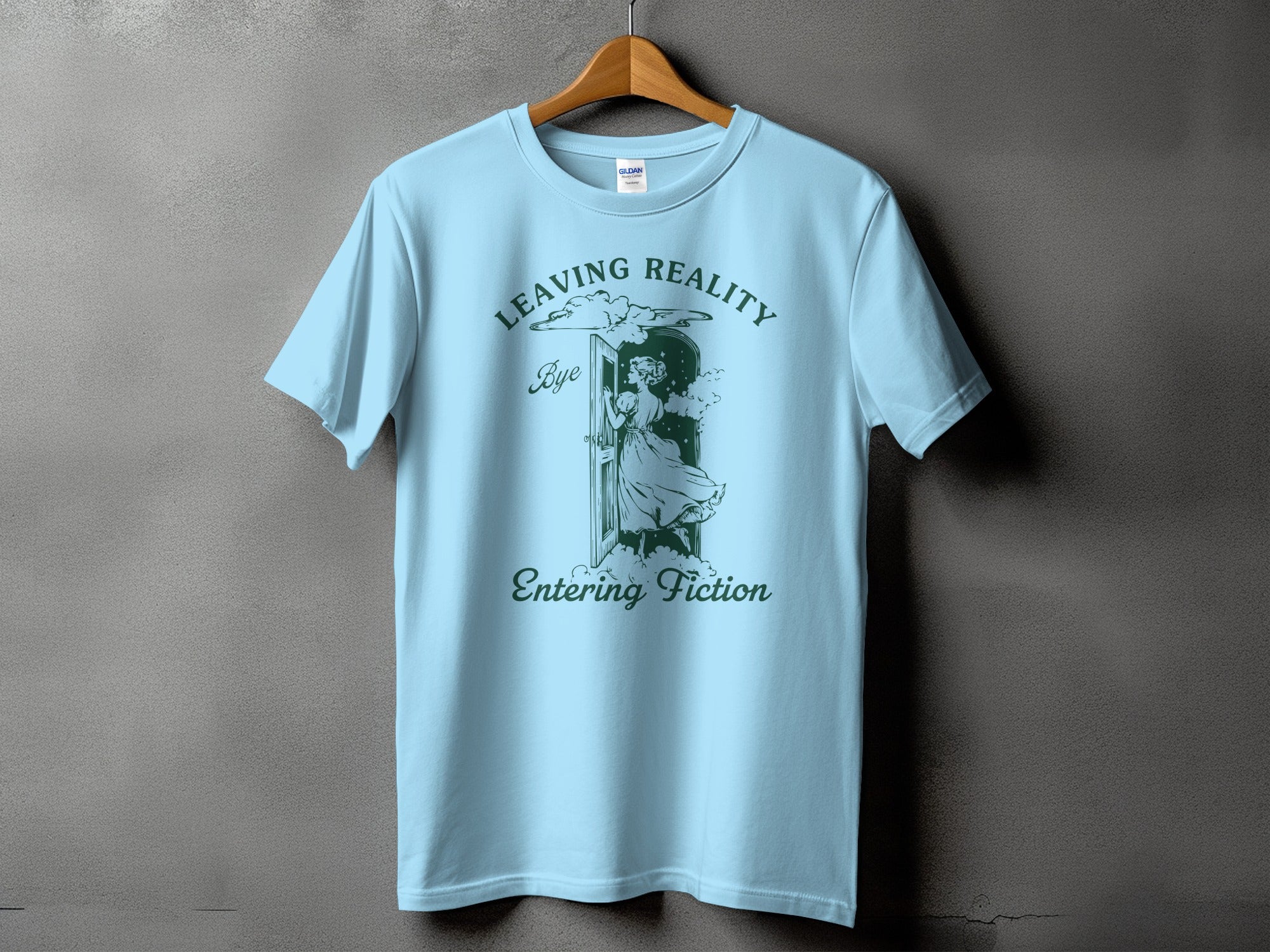 Light blue t-shirt with green text and graphic of a woman entering a doorway labeled "Leaving Reality, Bye, Entering Fiction".