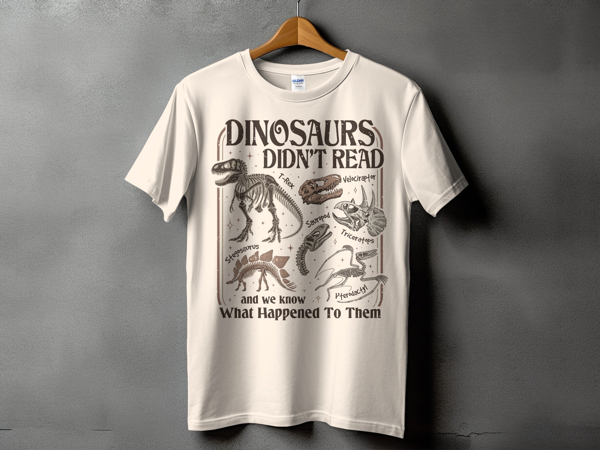Cream t-shirt with "Dinosaurs Didn't Read" and dinosaur skeletons and skulls.