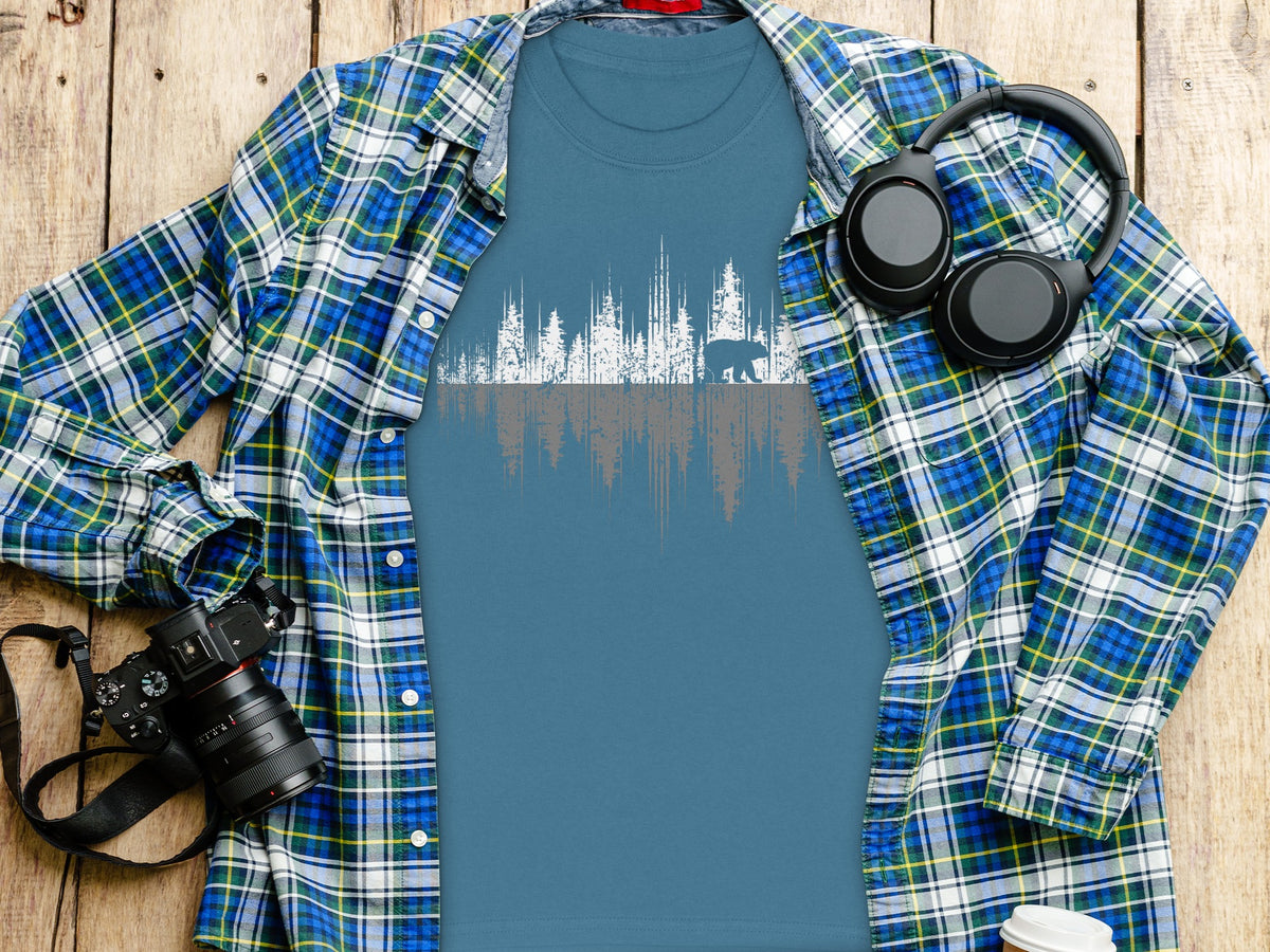 Blue t-shirt with white and grey forest and bear graphic, worn under plaid shirt.