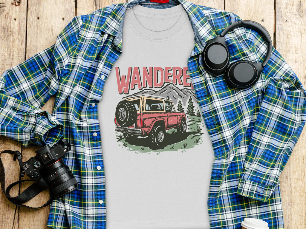T-shirt with "WANDERE" text and retro SUV graphic, over plaid shirt on wood.
