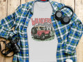 T-shirt with "WANDERE" text and retro SUV graphic, over plaid shirt on wood.