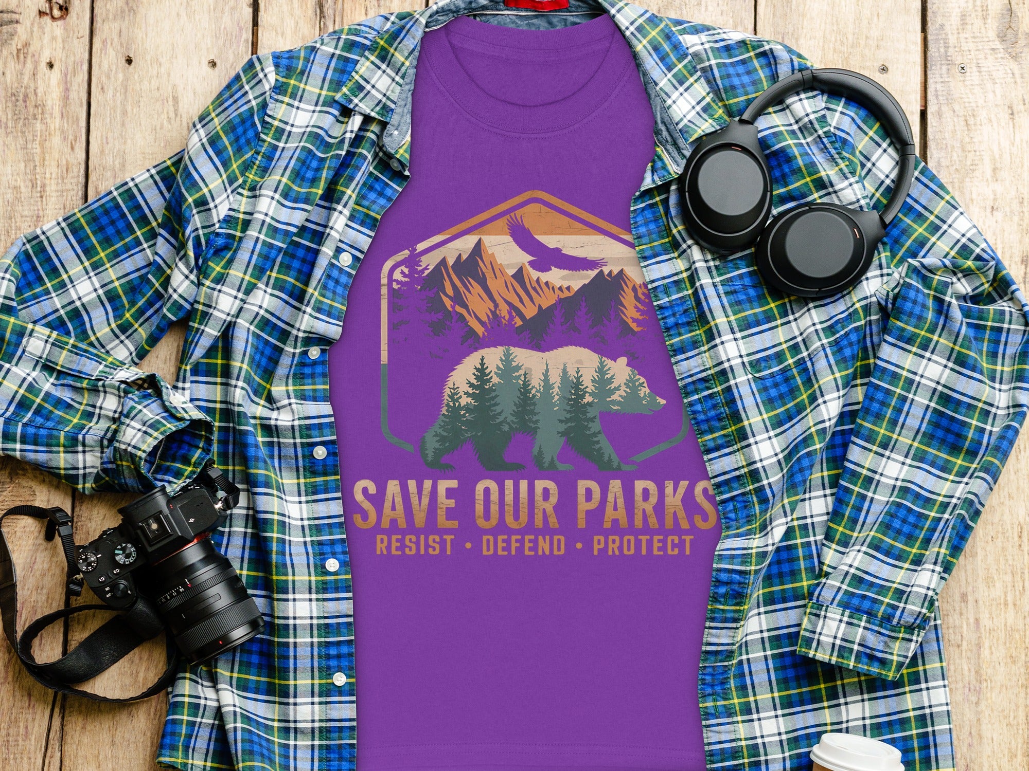 Purple t-shirt with bear and mountain graphic, text "SAVE OUR PARKS", laid flat with clothing and accessories.