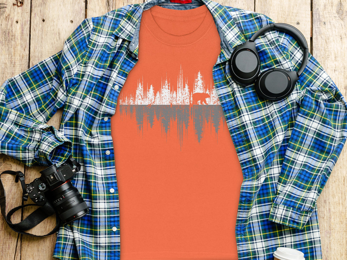 Orange t-shirt with white forest and bear graphic, layered under blue plaid shirt.